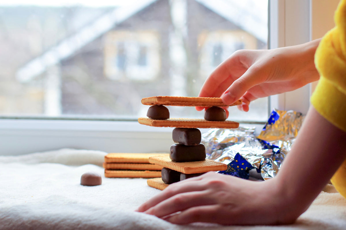Child stacking chocolates and wafers into a tower by a window