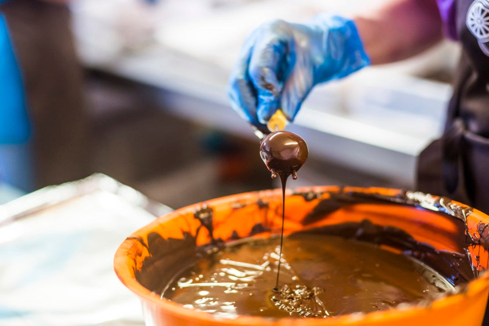 Gloved hand lifting a chocolate-dipped treat from a bowl of melted chocolate
