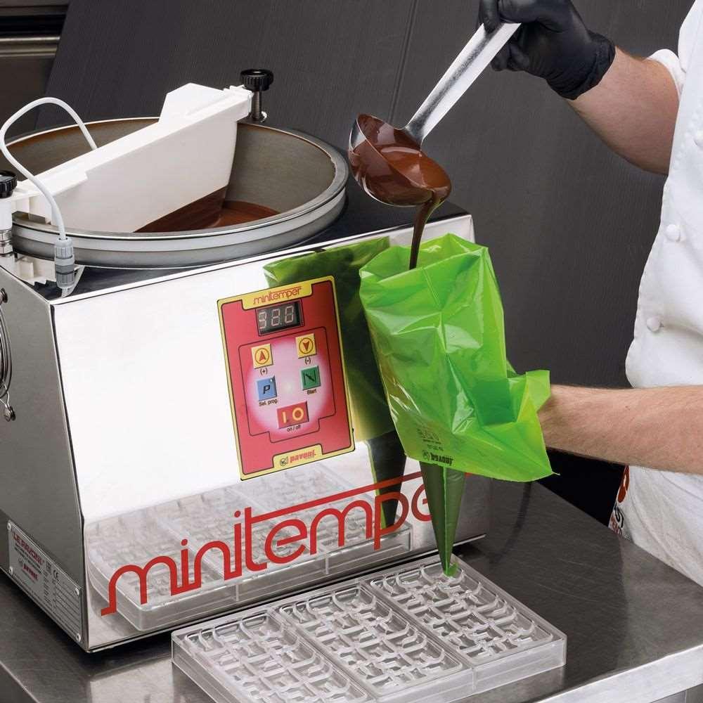 MiniTemper tempering machine with a hand filling a green piping bag with tempered chocolate over a mold