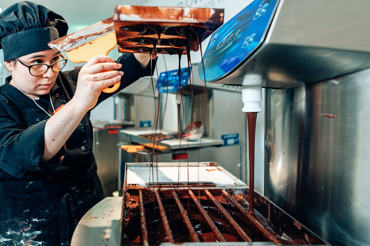 Chocolatier operating a professional chocolate moulding machine filling bar molds