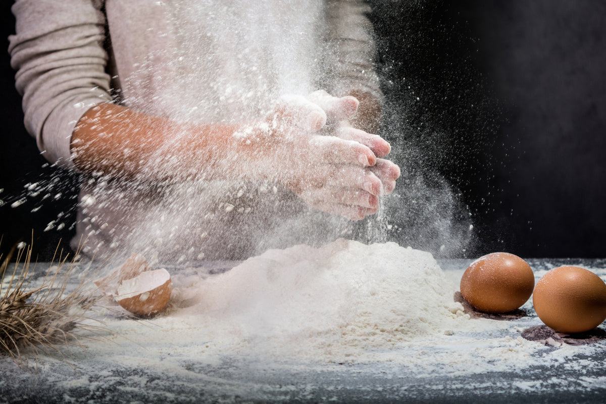Hands dusting flour over a work surface with eggs in the background