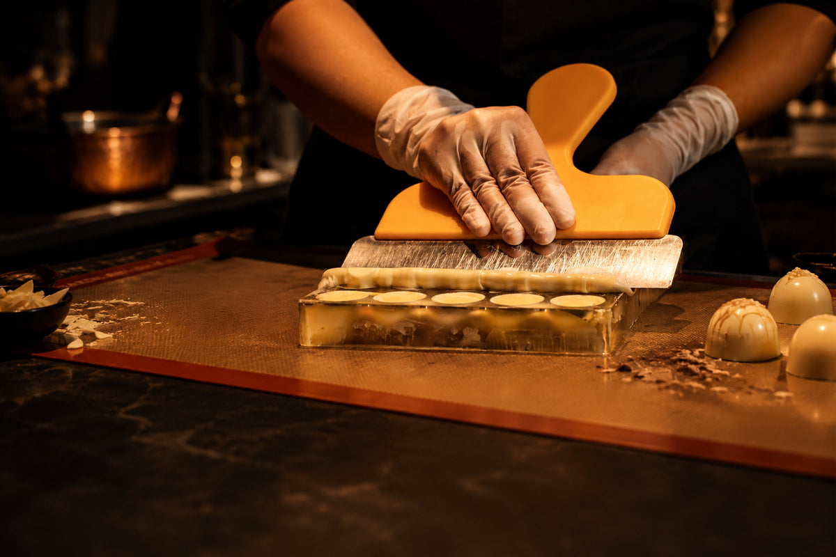 Chocolatier scraping a polycarbonate bonbon mould with an orange scraper