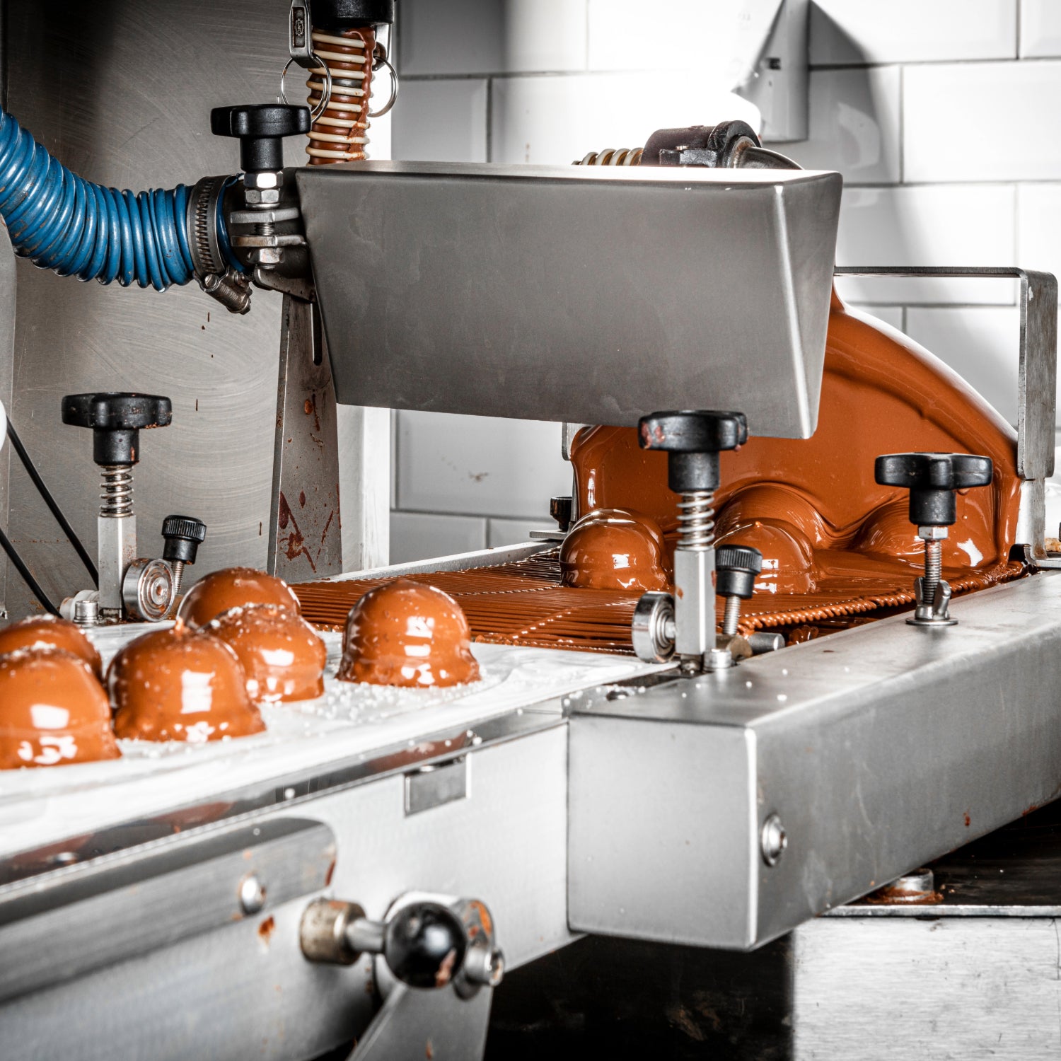 Chocolate World industrial chocolate enrobing machine coating pralines with tempered chocolate on continuous conveyor belt