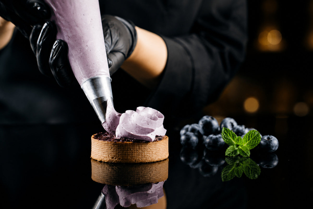 Piping violet cream onto a tartlet with blueberries and mint
