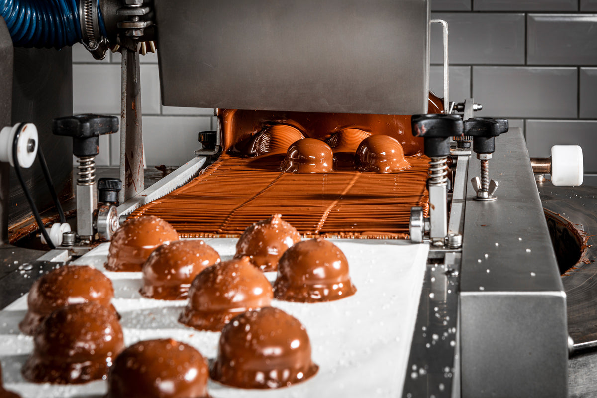 Chocolate domes leaving an enrobing machine on a conveyor belt